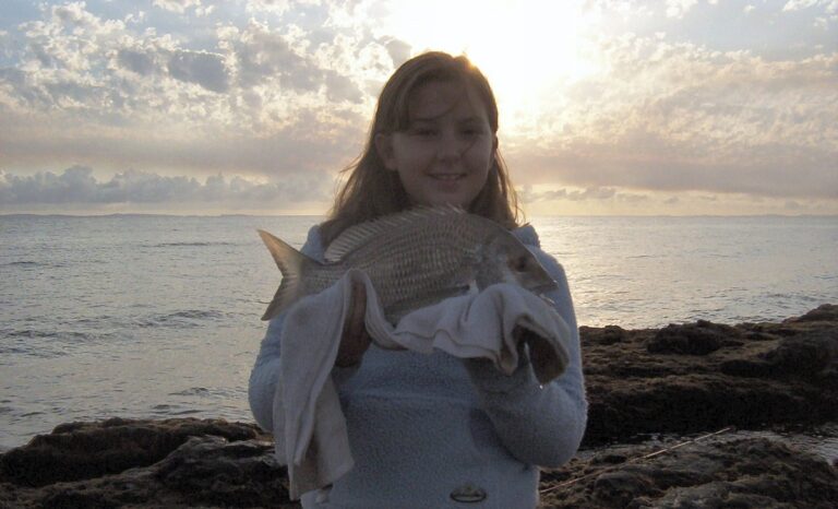 Young angler holding a yellowfin bream at sunrise on the rocks at Scotts Point, Moreton Bay, Queensland, just before releasing it
